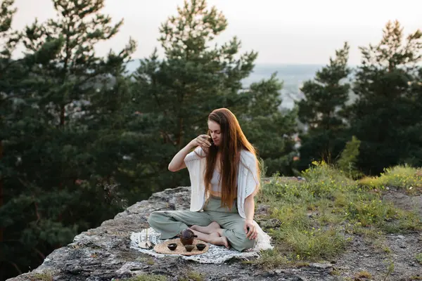 Gün batımında dağlarda çay seremonisi. Genç bir kadın doğada meditasyon yapar.