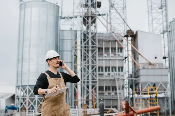 一位工程师在一个带有谷物的筒仓的背景下在工业区工作 — 图库照片