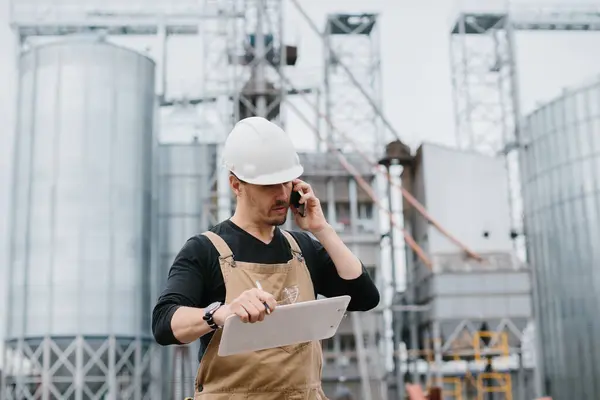 An engineer works in an industrial area on the background of a silo with grain.