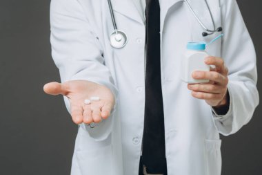 Steteskoplu, ceketli, elinde şişe ve haplarla kıdemli erkek doktor..