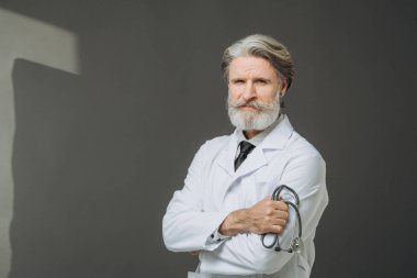 Elinde fallendoskop olan beyaz önlüklü kıdemli bir doktor gri arka planda poz veriyor. Sağlık ve Tıp Konsepti.
