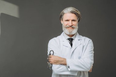 Elinde fallendoskop olan beyaz önlüklü kıdemli bir doktor gri arka planda poz veriyor. Sağlık ve Tıp Konsepti.