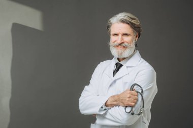 Elinde fallendoskop olan beyaz önlüklü kıdemli bir doktor gri arka planda poz veriyor. Sağlık ve Tıp Konsepti.