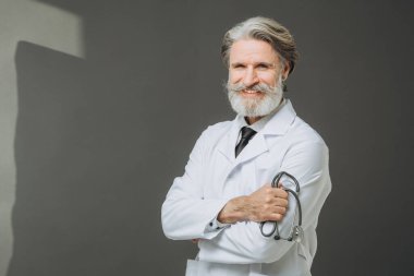 Elinde fallendoskop olan beyaz önlüklü kıdemli bir doktor gri arka planda poz veriyor. Sağlık ve Tıp Konsepti.