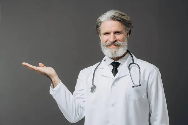 Ein Grauhaariger Arzt Weißen Arztkittel Zeigt Einen Leeren Raum lizenzfreie Stockbilder