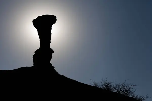 Backlit silhouette of a geological formation against the background of a blue sky. This geological formation blocks the sun and creates a halo of glare that produces a black silhouette.