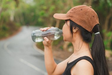 Kadın koşucu sokakta su içiyor.