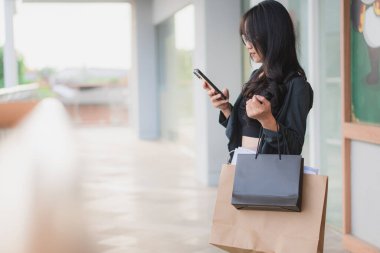 Alışveriş çantalı ve akıllı telefonlu bir kadın alışveriş merkezinin yakınında yürüyor..