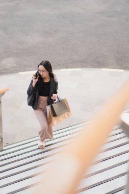 Alışveriş çantalı ve akıllı telefonlu bir kadın alışveriş merkezinin yakınında yürüyor..