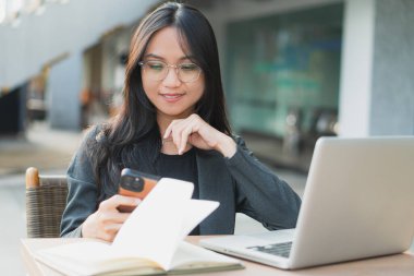 Ofis masasında otururken akıllı telefonunu kullanan kendine güvenen genç bir iş kadını..