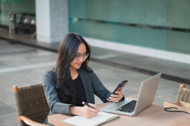 Ofis masasında otururken akıllı telefonunu kullanan kendine güvenen genç bir iş kadını..