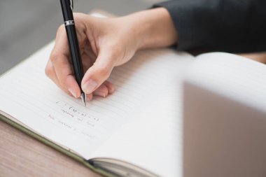 Beyaz ahşap masadaki defterde yazıyor.