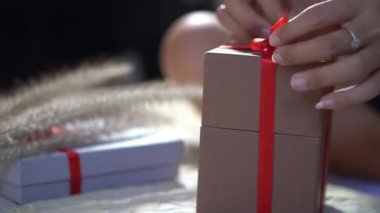 Kadın eli kırmızı kurdeleyi bağlarken Noel hediyesini paketliyor
