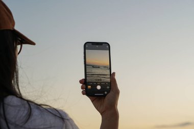 Gün batımında kumsalda akıllı telefon kullanan genç bir kadın..