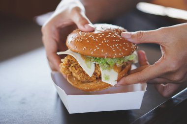 close - up of hand of a person holding chicken burger with lettuce and fried chicken on the table in the restaurant