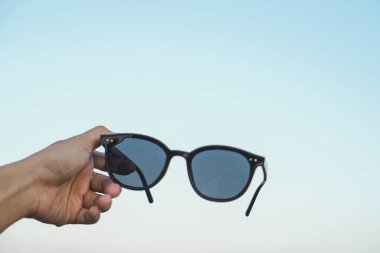 Güneş ve güneş gözlükleriyle mavi gökyüzünü tutan kadın.