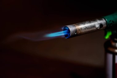 Koyu bir arkaplanda mavi bir alevle yanan bir kaynak makinesinin yakın çekimi.