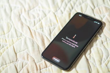 Kullanılmadan önce serinlemesi gerektiğini belirten sıcaklık uyarısı içeren bir akıllı telefon. Telefon örtülü kumaş bir yüzeye yerleştiriliyor..
