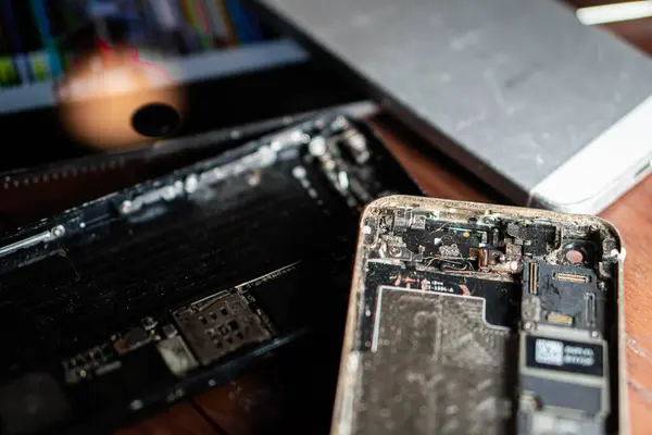 Ahşap bir yüzey üzerinde görünür iç bileşenleri olan parçalanmış akıllı telefonlara yakın çekim.