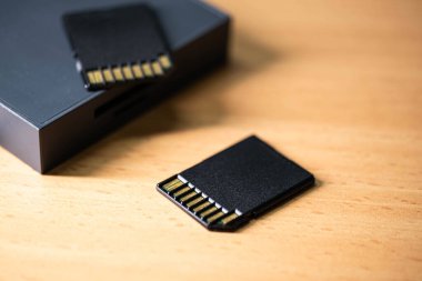 Tahta bir yüzeyde iki SD kartın yakın plan görüntüsü, bir tanesi de siyah kart okuyucusuna yerleştirilmiş..