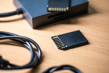 SD hafıza kartlarına ve tahta bir yüzeyde kart okuyucuya yakın çekim. Ön planda siyah bir kablo da görünür..