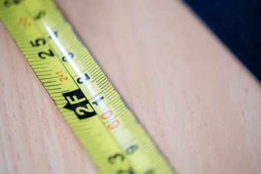 Metal bir cetvelin yanındaki ahşap masaya sarı ve siyah şeritli bir mezura..