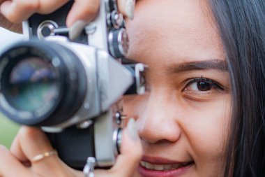 Gözüne antika bir kamera tutarak fotoğraf çekmeye odaklanan bir kadının yakın çekimi. Arka plan bulanık, yüzünü ve kamerasını vurguluyor..
