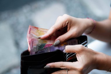 Siyah bir cüzdan tutan ve Endonezya Rupia banknotlarını sayan biri..
