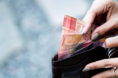 Endonezya rupia banknotlarını tutan ve bir cüzdana koyan biri. Adamın manikürlü tırnakları var..