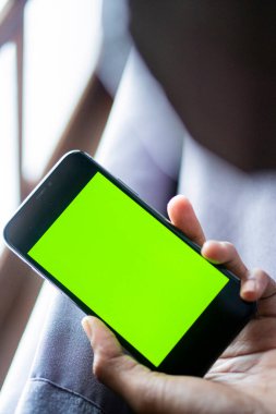 Elinde parlak yeşil ekranlı akıllı bir telefon tutan kişi, bir kanepede oturuyor..