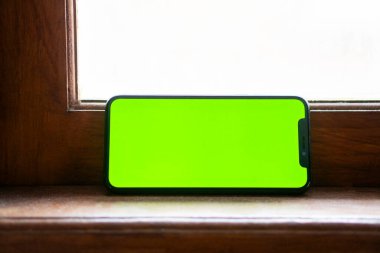 Ahşap pencere pervazına yatay yerleştirilmiş yeşil ekranlı akıllı bir telefon..