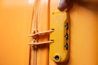 Sarı bir bavula şifreli kilit takan birinin yakın çekimi..