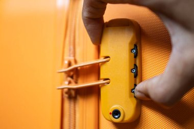 Sarı bir bavula şifreli kilit takan birinin yakın çekimi..