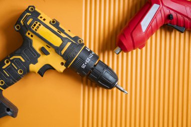 Sarı ve siyah kablosuz matkap ve turuncu desenli bir yüzey üzerinde kırmızı kablosuz tornavida..