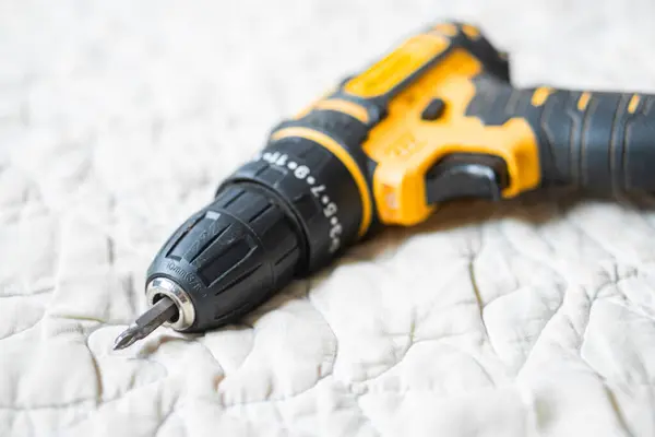 Örtülü kumaş bir yüzeye yerleştirilmiş sarı ve siyah desenli kablosuz bir matkabın yakın çekimi..