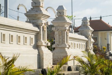 Geleneksel taş bir duvar, karmaşık oymalar ve dekoratif sütunlarla, arka planda bitkiler ve bir bina olan açık hava ortamında inşa edilmiş..