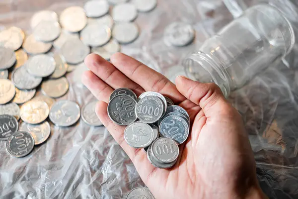 Birkaç Güney Kore sikkesi ve arka planda boş bir cam kavanoz tutan bir el..