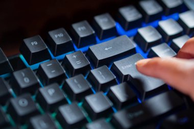 Bir kişinin parmağının arkadan aydınlatılan mekanik klavyede Enter tuşuna basarken yakın plan görüntüsü.