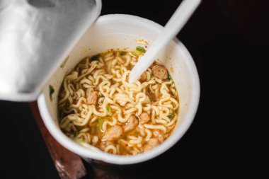 Plastik çatallı bir fincan hazır erişte. Erişteler et ve sebze parçalarıyla birlikte et suyunun içinde..