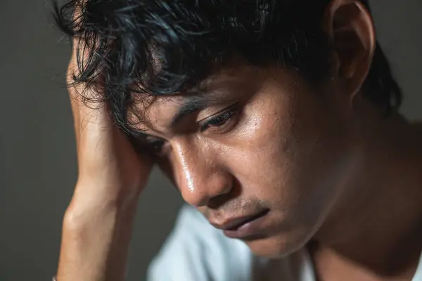 Sıkıntılı bir yüz ifadesi olan, tek eliyle başını tutan birinin yakın çekimi. Arka plan koyu renkli, kişinin duygusal durumunu vurguluyor..