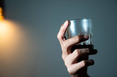 Karanlık bir içecekle bardağı tutan el, loş bir arka planda..