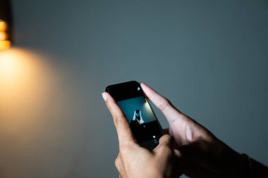 Akıllı bir telefonu tutan ve loş bir odada fotoğraf çeken ellerin yakın çekimi..