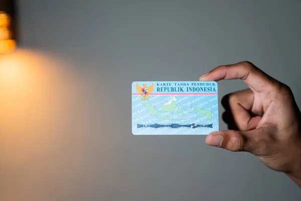Sade bir arkaplanda Endonezya kimlik kartı tutan biri..