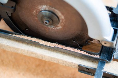 Bir tahta parçasını kesen dairesel bir testerenin yakın çekimi. Bıçağın etrafında talaş var..