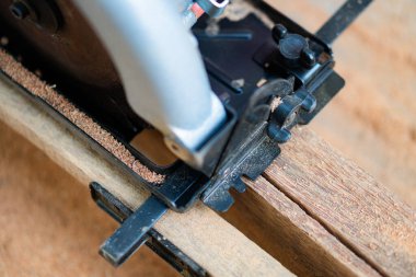 Tahta bir tahtayı kesen dairesel bir testerenin yakın çekimi, görünürde talaş var..