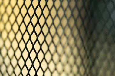 Bulanık sarı arkaplanı olan siyah metal bir tel örgüye yakın plan..