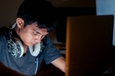 Genç adam, boynunda kulaklıkla dizüstü bilgisayara odaklanmış..