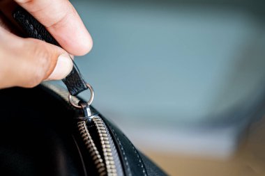 Siyah deri bir çantanın fermuarını tutan bir elin yakın çekimi..