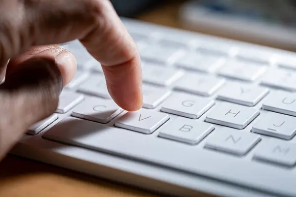 Beyaz bir bilgisayar klavyesindeki 'V' tuşuna basan kişinin yakın plan görüntüsü.