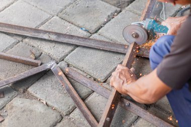 Asfaltlı bir yüzey üzerindeki metal parmaklıkları kesmek için açı öğütücü kullanan bir kişi.